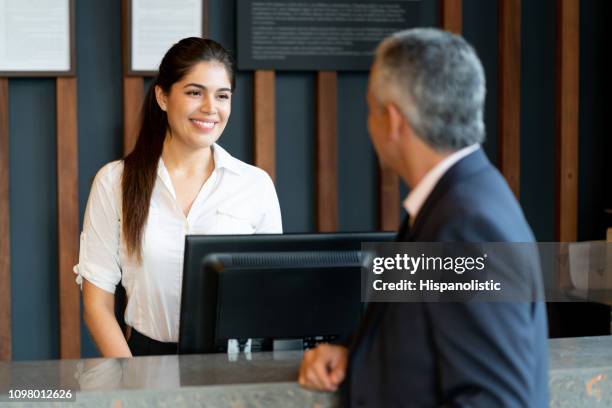 beautiful hotel receptionist standing behind counter talking to male guest smiling - hotel concierge stock pictures, royalty-free photos & images