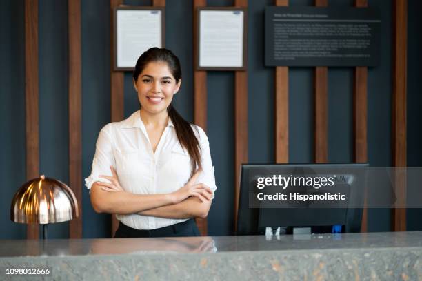 beautiful hotel manager stading behind check in counter smiling at camera with arms crossed - recepção de hotel imagens e fotografias de stock