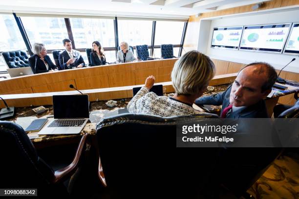 businesswoman and businessman whispering on the opposite table of a conference room - microphone debate stock pictures, royalty-free photos & images