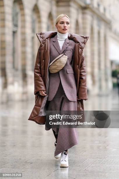 Guest wears a brown long puffer coat, a Balenciaga fanny pack bag, a checked blazer jacket, a white turtleneck, outside Alexis Mabille, during Paris...