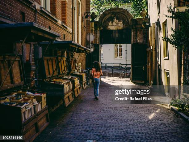 young lady walking along alley wiith bookstores on its side - book shop stock pictures, royalty-free photos & images