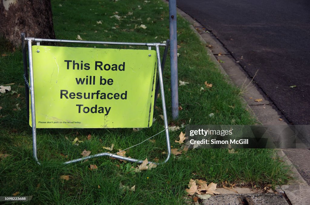 Sign stating 'This road will be resurfaced today' beside a suburban road