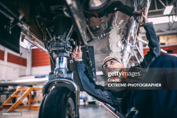 ältere weibliche ingenieur mit einem steckschlüssel während der reparatur oder wartungsarbeiten bis zum fahrwerk ein kleines flugzeug in eine wartungshalle - landing gear stock-fotos und bilder