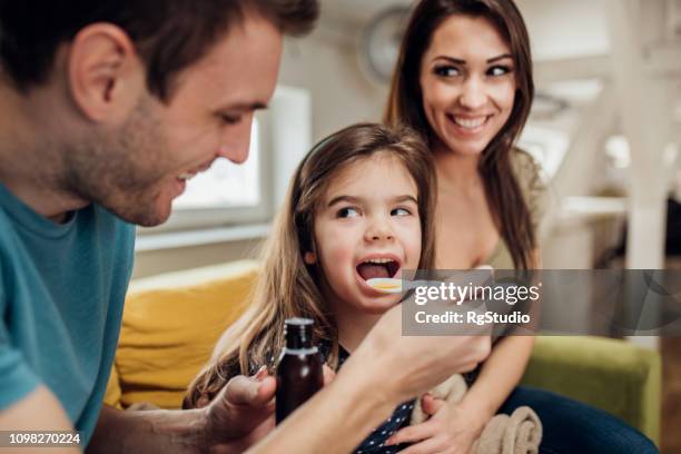 parents giving their daughter a syrup - cough syrup stock pictures, royalty-free photos & images