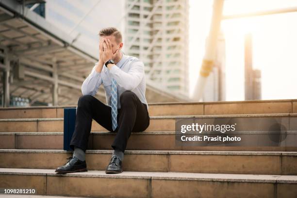 young business man crying abandoned lost in depression sitting on ground street concrete stairs suffering emotional pain, sadness, looking sick in grunge lighting - hombre llorando fotografías e imágenes de stock