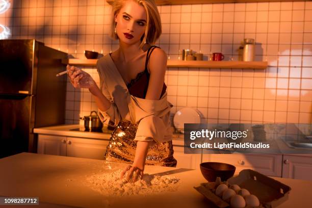 beautiful housewife smoking cigarette while cooking in kitchen with orange light