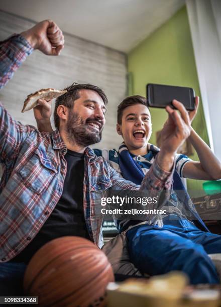 happy son and father cheering on basketball team and watching game at home - watching basketball stock pictures, royalty-free photos & images