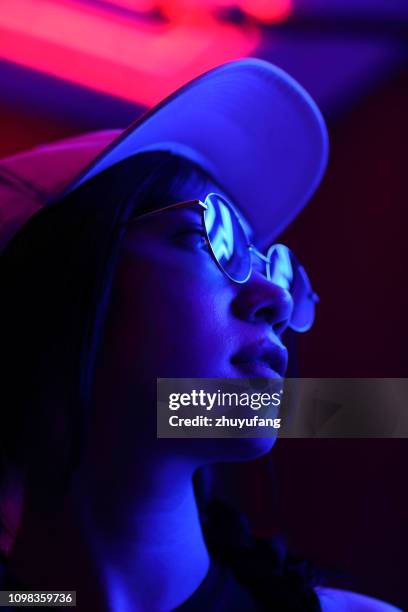 close-up portrait of young woman wearing sunglasses in darkroom - neon colored 個照片及圖片檔