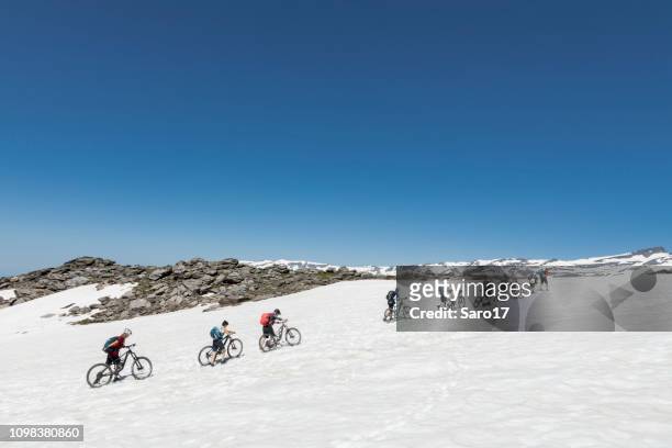 mountainbikers crossing snow field at andalucian sierra nevada, spain. - andalucian sierra nevada stock pictures, royalty-free photos & images