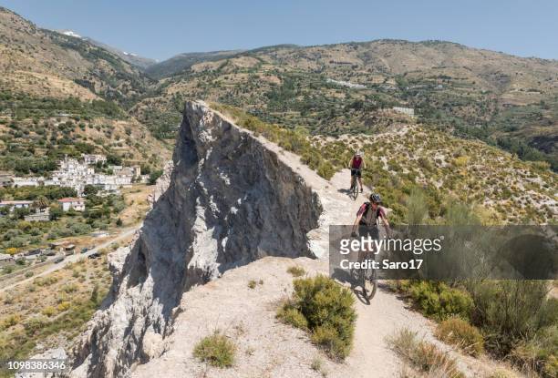 couple of mountainbikers on a single trail nearby a cliff at andalucian sierra nevada, spain. - andalucian sierra nevada stock pictures, royalty-free photos & images