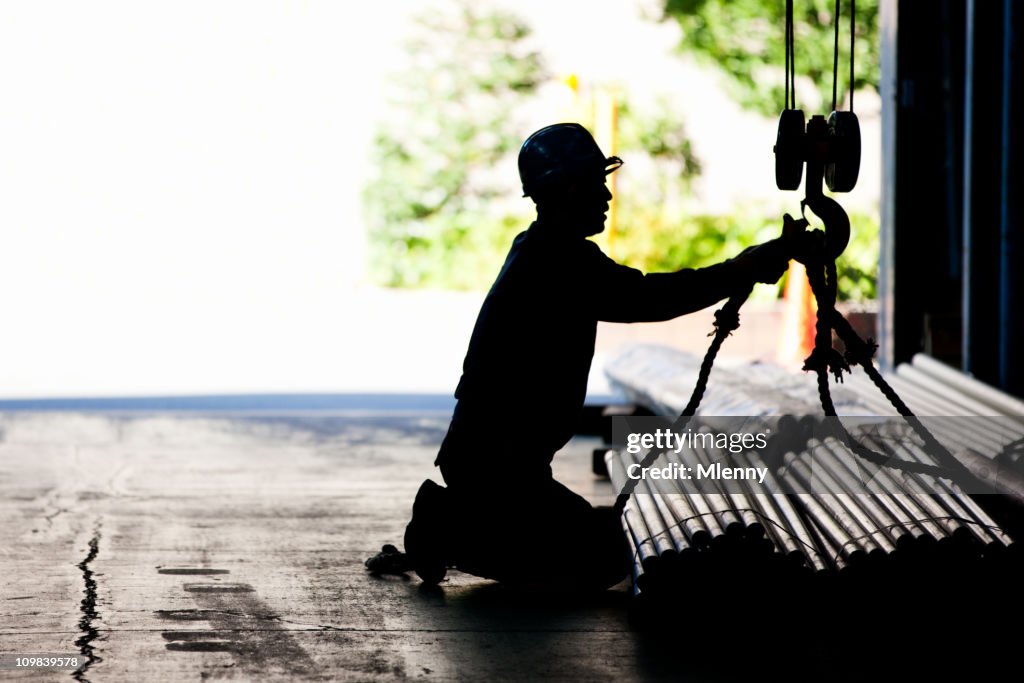 Steel worker tying metal tubes to crane jib in warehouse