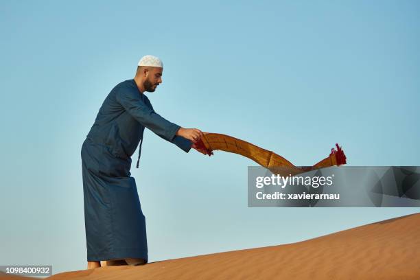 mid adult man spreading prayer mat on sand - prayer mat stock pictures, royalty-free photos & images