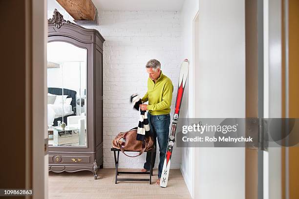 mature man packing a bag with skis leaning on wall - ski pants stockfoto's en -beelden