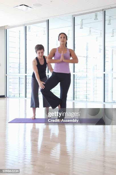 yoga instructor helps woman with pose - yoga instructor stock pictures, royalty-free photos & images