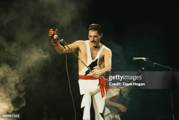 Singer Freddie Mercury performing on stage with British rock group Queen, 1985. Guitarist Brian May is in the background.