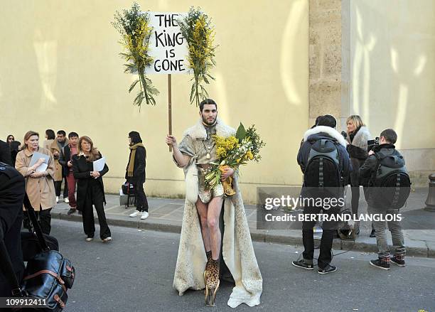 Man holds a sign reading "The king is gone" and flowers, in front of the gardens of the Rodin Museum where the Autumn/Winter 2011-2012 ready-to-wear...