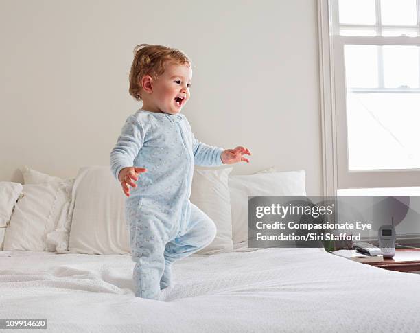 smiling baby walking on bed - baby first steps stock-fotos und bilder