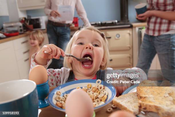 family in kitchen, girl at table eating breakfast - baby feeding fotografías e imágenes de stock