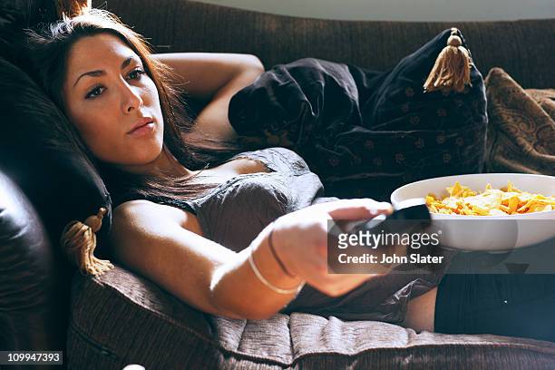 young woman using remote control on sofa - couch potato imagens e fotografias de stock