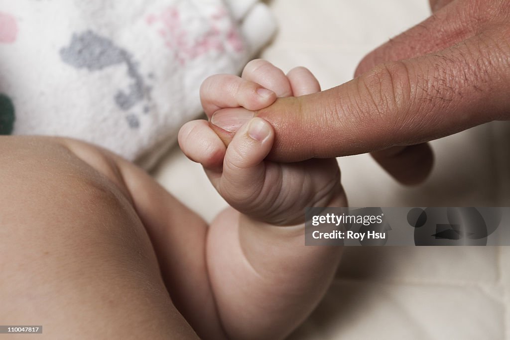 New born baby girl grabbing adult finger