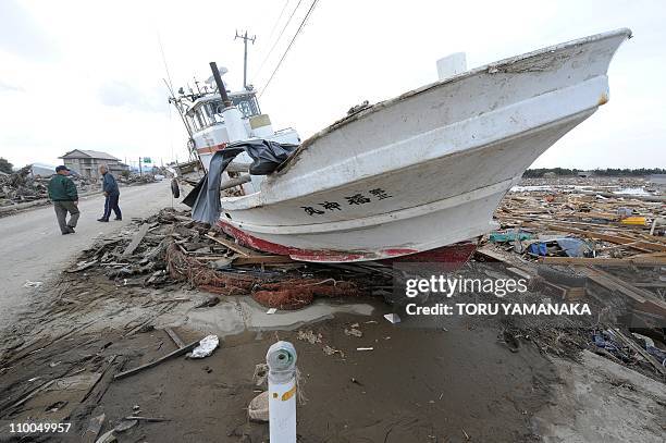 Local residents walk beside a fishing boat that was thrown onto the road by the tsunami, close to the sea front, in Natori, Miyagi Prefecture, on...