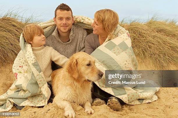 family with dog, under quilt, on beach - one in three people stock pictures, royalty-free photos & images