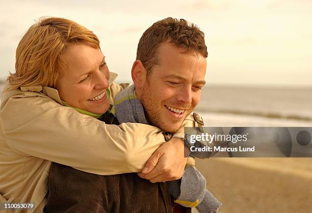 woman embracing man from behind on beach - walberswick stock pictures, royalty-free photos & images