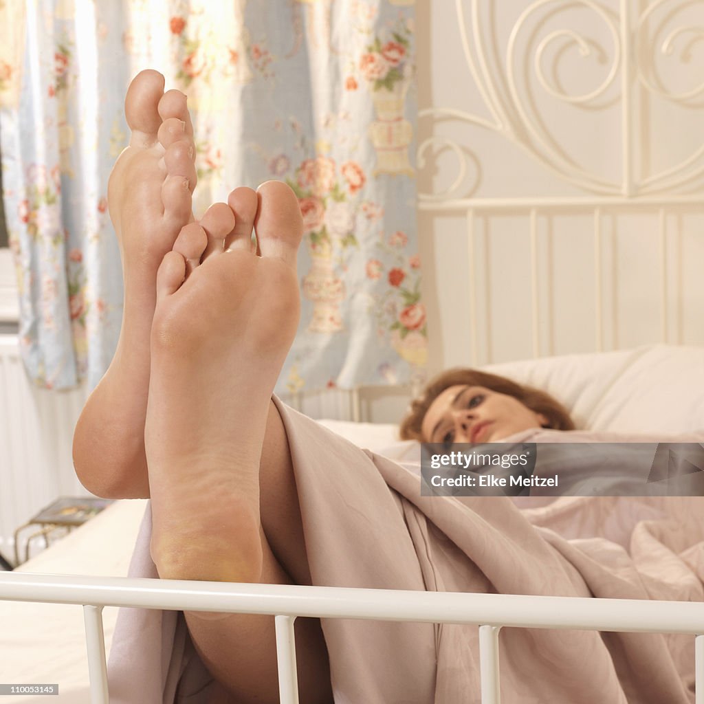 Young woman in bed with feet up