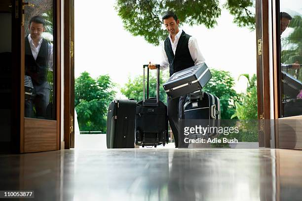 man carrying suitcases into hotel - carry on luggage photos et images de collection