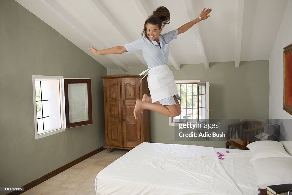 Hotel maid jumping on bed in room
