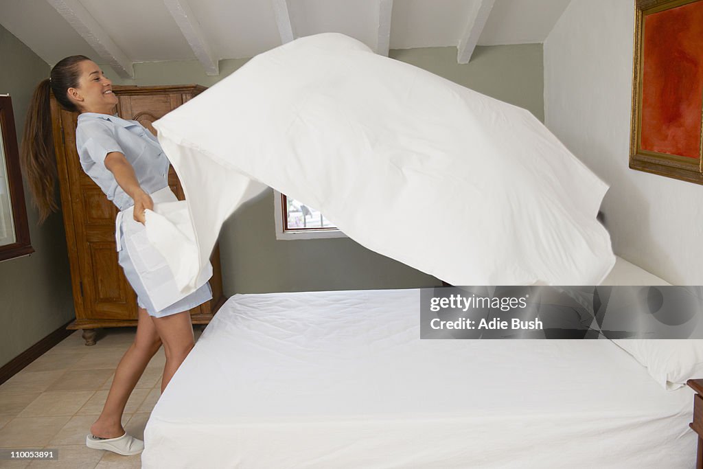 Hotel maid putting throwing sheet on bed