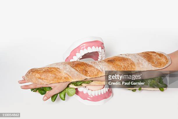 a submarine sandwich with a human arm in it being bitten fake teeth - cannibalism stock pictures, royalty-free photos & images