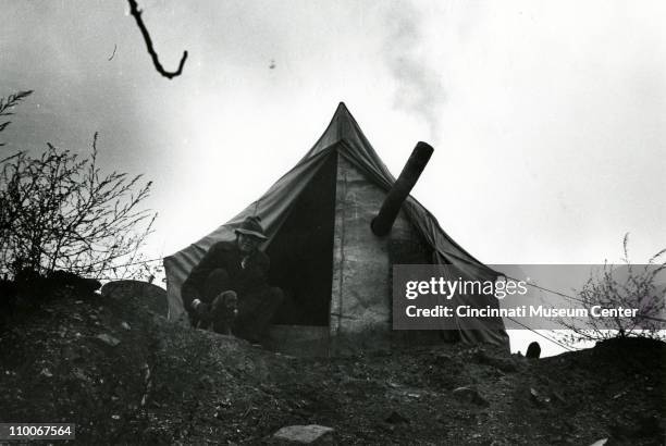 Portrait of an unidentified man as he sits in the entrance to a tent at the top of an inline, along Ohio River, Cincinnati, Ohio, December 1935.