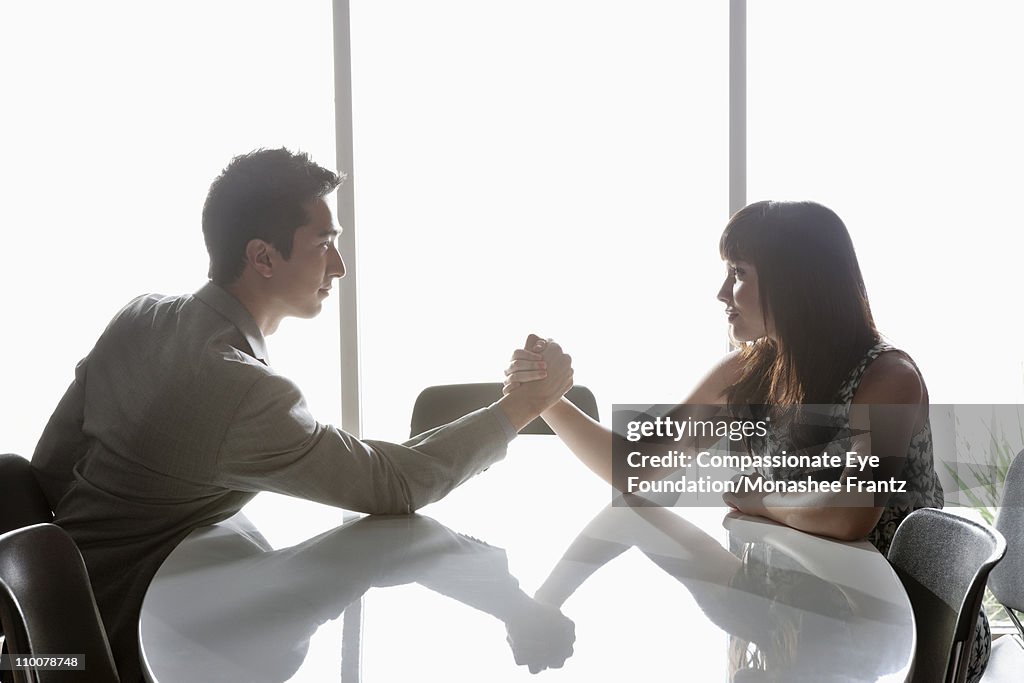 Man and woman arm wrestling at boardroom table.