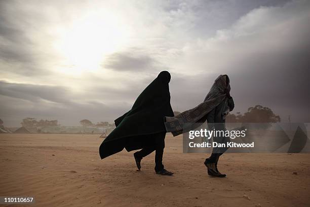 Two men walk through a United Nations displacement camp during a huge sandstorm on March 15, 2011 in Ras Jdir, Tunisia. As fighting continues in and...