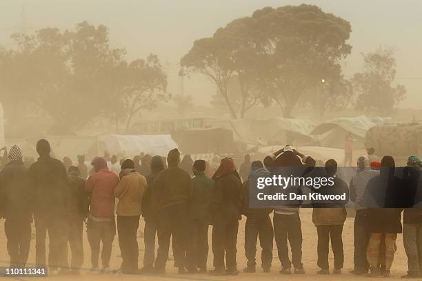 Men queue for food during a sandstorm at a United Nations displacement camp on March 15, 2011 in Ras Jdir, Tunisia. As fighting continues in and...