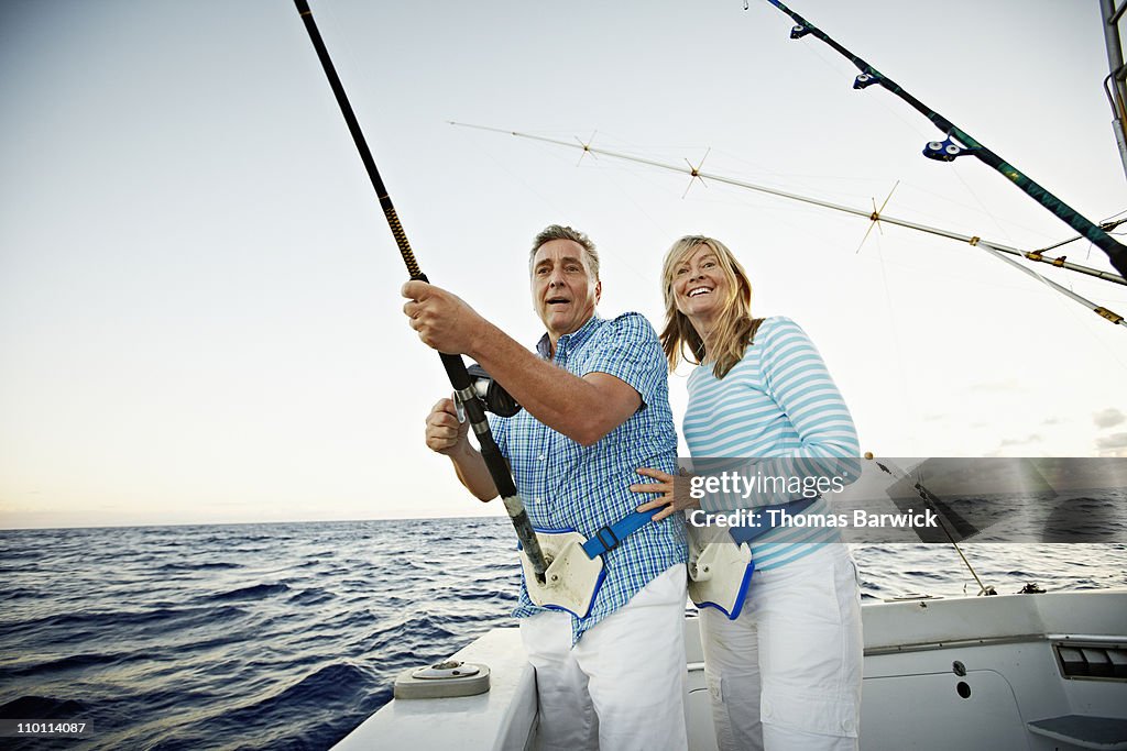 Senior couple reeling in fish on fishing boat