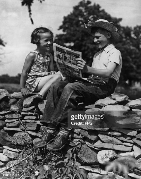 Boy and a girl sitting on a wall and looking at a comic, USA, circa 1935. The comic features a Dick Tracy story.