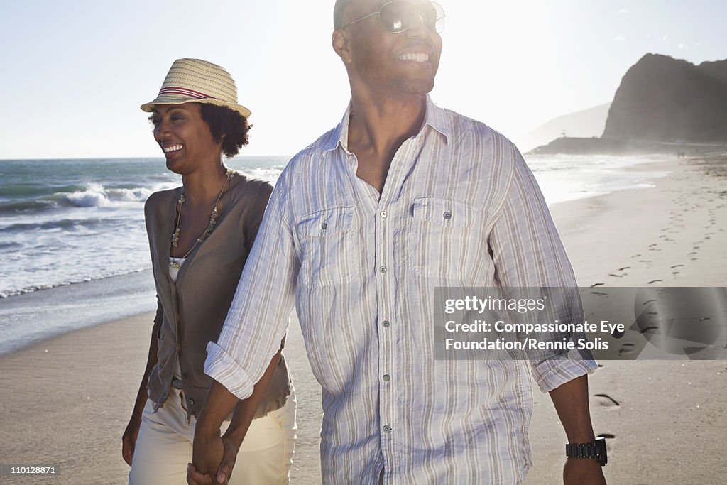 Smiling couple walking hand in hand down the beach