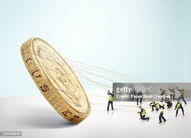 group of builders carrying a large gold pound coin - miniature stock-fotos und bilder