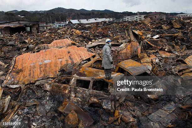 Rescue worker stands on top of a burned vehicle looking for more bodies hidden amongst the rubble of a village destroyed by the devastating...