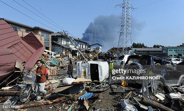 Local residents walk on a street covered with collapsed houses and damaged vehicles in Tagajo, Miyagi prefecture on March 13, 2011 following a...