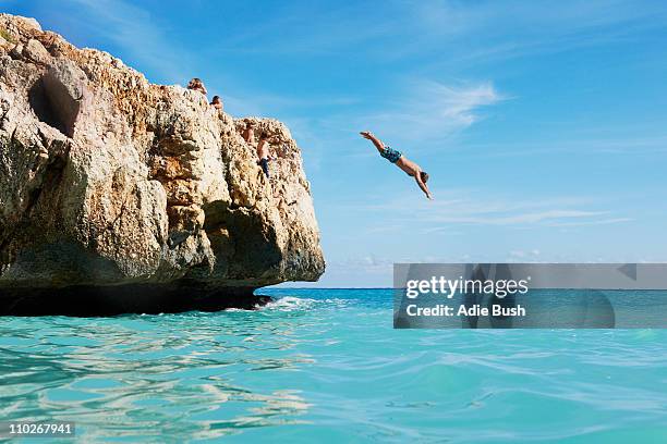 man diving from rocks into the sea - diver imagens e fotografias de stock