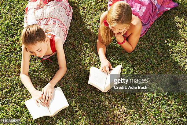girls lying on grass reading books - happy tween girls lying on grass stock pictures, royalty-free photos & images