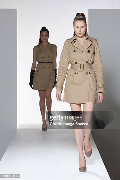 two models wearing beige dress and mackintosh on catwalk at fashion show - fashion show stockfoto's en -beelden