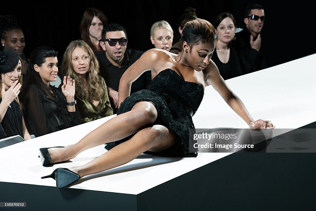 Model sitting on catwalk having fallen down at fashion show