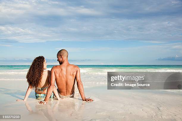 couple sitting on sandy beach at water's edge - indian honeymoon couples stock pictures, royalty-free photos & images