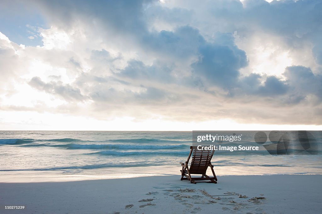 Deck chair on sandy beach at water's edge