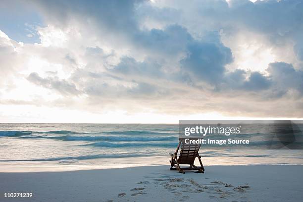 deck chair on sandy beach at water's edge - dusk clouds stock pictures, royalty-free photos & images