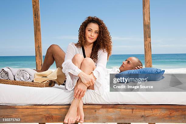 paar auf dem bett am sandstrand urlaub - junge frau bett sitzen blick in die kamera stock-fotos und bilder